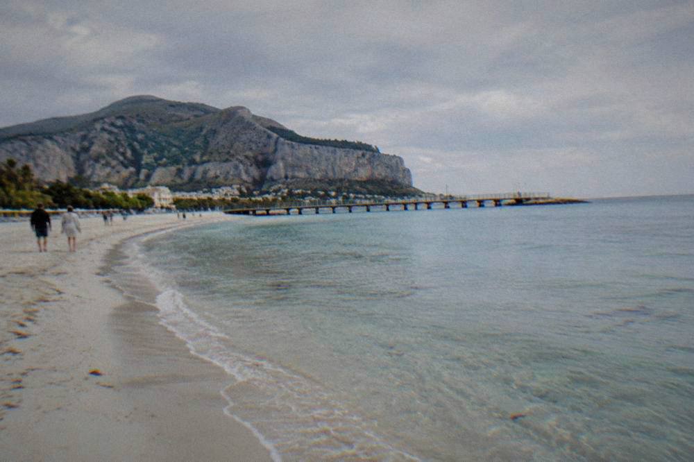 A long sandy beach with a curved pier and clear shallow water under a wide sky